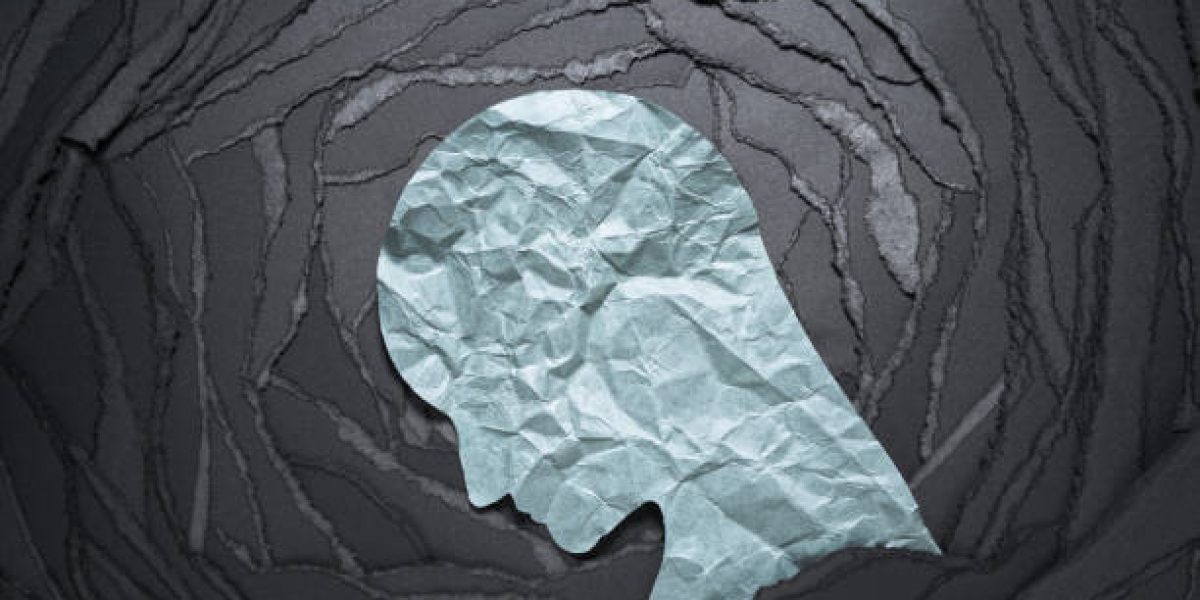Negative emotion image. Person head shaped paper on black torn paper background.